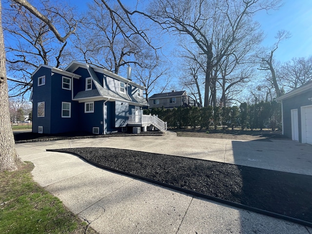 view of side of property with a shingled roof, driveway, a chimney, and a gambrel roof