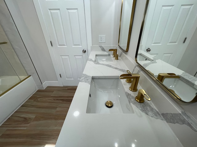 bathroom featuring double vanity, combined bath / shower with glass door, a sink, and wood finished floors