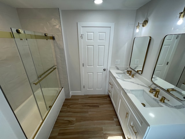 full bath with wood finished floors, bath / shower combo with glass door, double vanity, and a sink