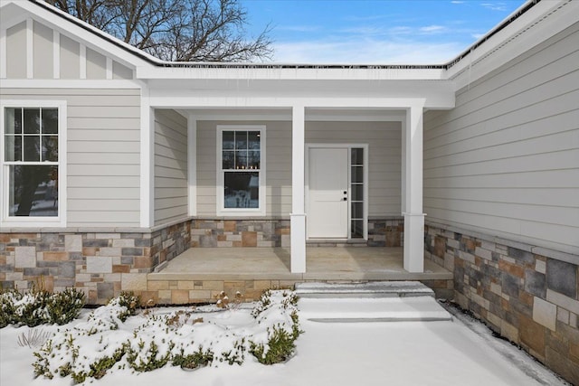 snow covered property entrance featuring stone siding, a porch, and board and batten siding