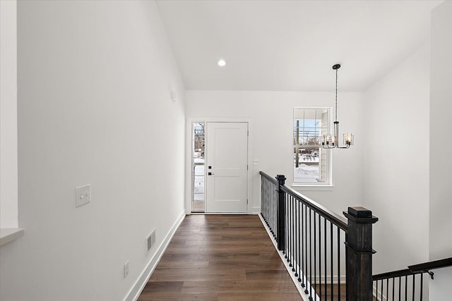 hallway featuring baseboards, visible vents, dark wood-style floors, an upstairs landing, and a notable chandelier