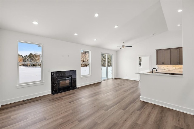 unfurnished living room featuring a high end fireplace, vaulted ceiling, baseboards, and wood finished floors