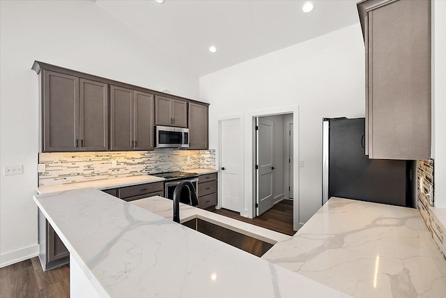 kitchen featuring stainless steel appliances, a sink, a peninsula, and light stone countertops