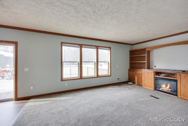 unfurnished living room with visible vents, ornamental molding, a wealth of natural light, and a glass covered fireplace