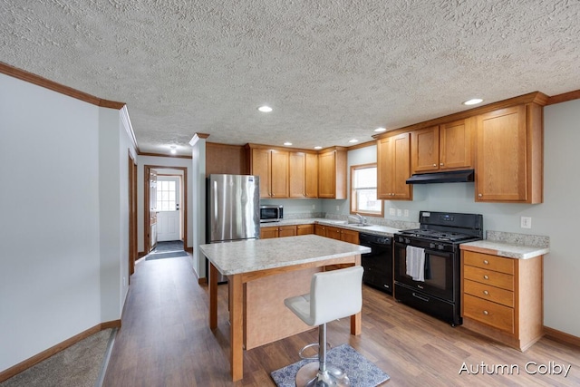 kitchen with a breakfast bar area, light countertops, a kitchen island, under cabinet range hood, and black appliances