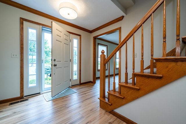 foyer with crown molding, light wood-type flooring, visible vents, and plenty of natural light