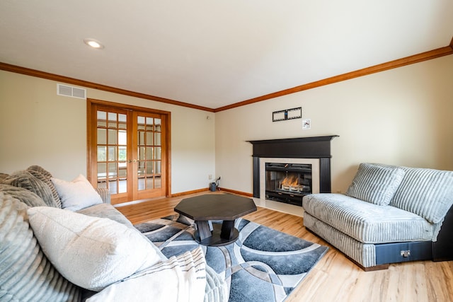 living room with a fireplace with flush hearth, visible vents, light wood-style floors, french doors, and crown molding