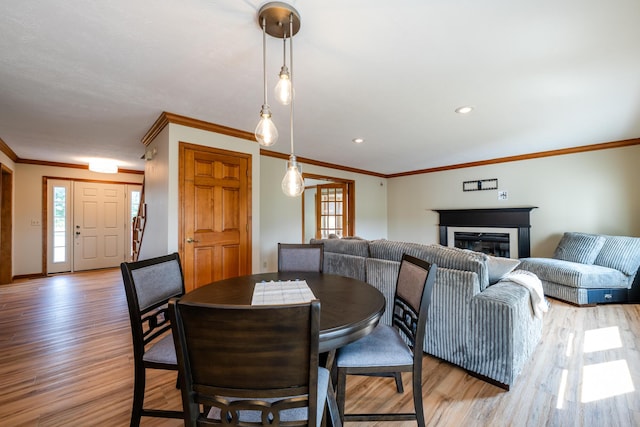 dining area with baseboards, light wood-type flooring, a glass covered fireplace, and crown molding