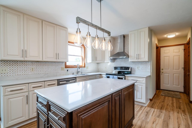 kitchen featuring hanging light fixtures, appliances with stainless steel finishes, dark brown cabinetry, a sink, and wall chimney exhaust hood