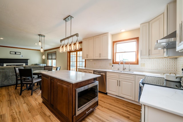 kitchen featuring open floor plan, stainless steel appliances, pendant lighting, a sink, and exhaust hood