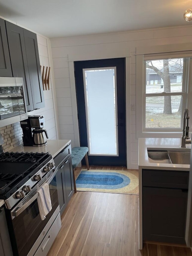 kitchen with light wood-style flooring, a sink, light countertops, tasteful backsplash, and gas range