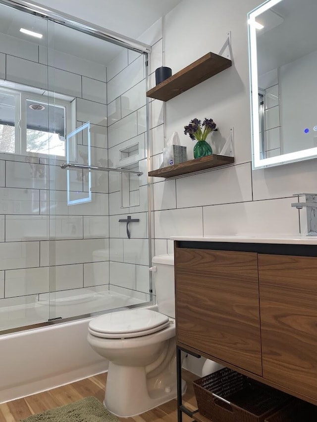 full bath with toilet, bath / shower combo with glass door, wood finished floors, and vanity