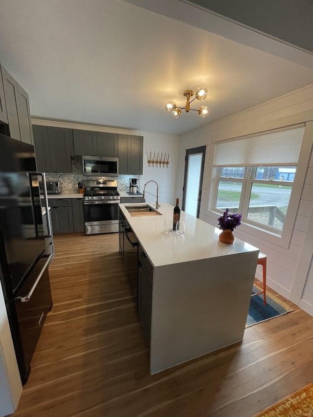 kitchen with a center island with sink, dark wood finished floors, stainless steel appliances, light countertops, and a sink