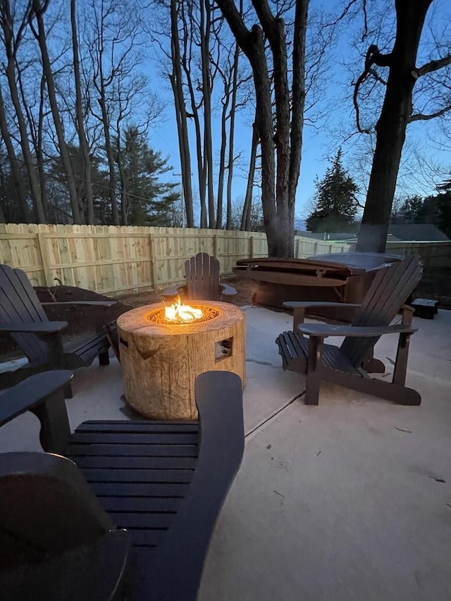 patio terrace at dusk featuring an outdoor fire pit, fence, and a jacuzzi