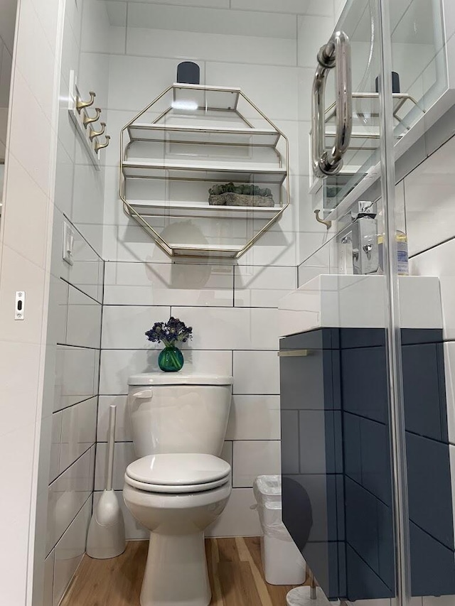 bathroom with wood finished floors, toilet, and tile walls