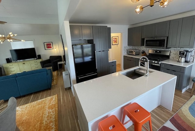 kitchen with an island with sink, appliances with stainless steel finishes, open floor plan, an inviting chandelier, and light countertops