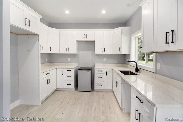 kitchen featuring light wood-type flooring, a sink, refrigerator, white cabinets, and light stone countertops