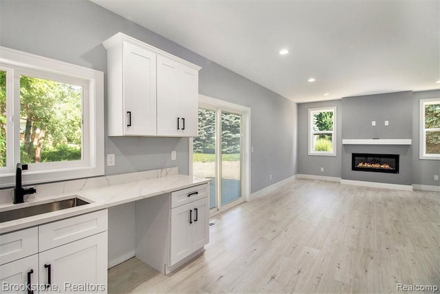 kitchen with a sink, white cabinetry, a wealth of natural light, and light wood finished floors