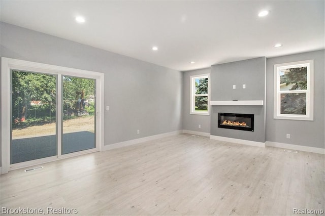 unfurnished living room featuring visible vents, baseboards, recessed lighting, light wood-style floors, and a glass covered fireplace