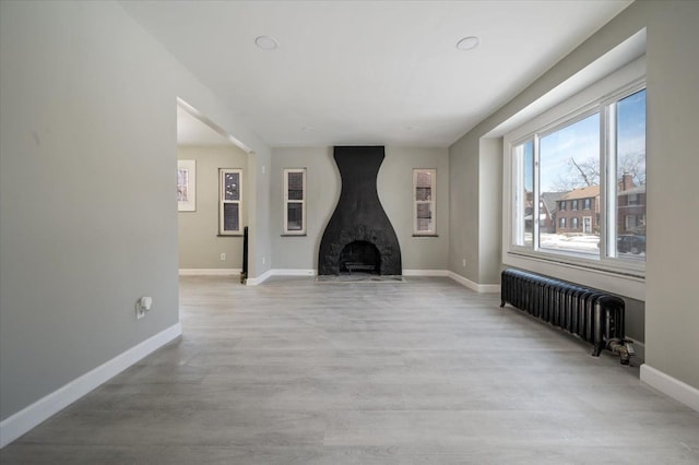 unfurnished living room featuring a high end fireplace, baseboards, light wood-style flooring, and radiator heating unit