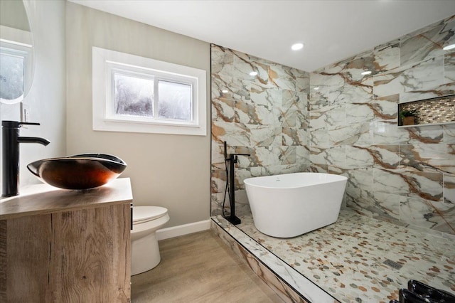 bathroom with baseboards, toilet, wood finished floors, a freestanding bath, and vanity