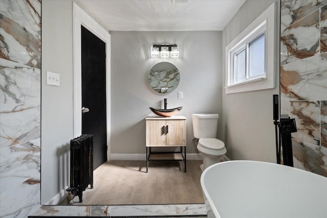 bathroom with a freestanding tub, toilet, wood finished floors, baseboards, and radiator