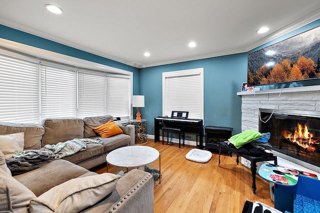 living room with recessed lighting, crown molding, a stone fireplace, and light wood finished floors