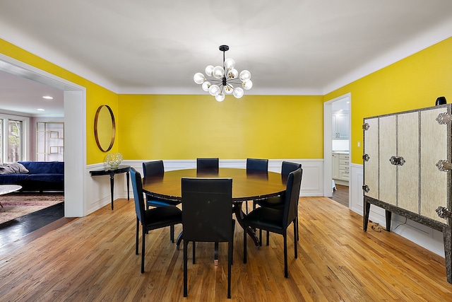 dining space with light wood-type flooring, a wainscoted wall, a decorative wall, and an inviting chandelier