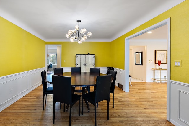 dining space with a wainscoted wall, light wood-style flooring, and an inviting chandelier