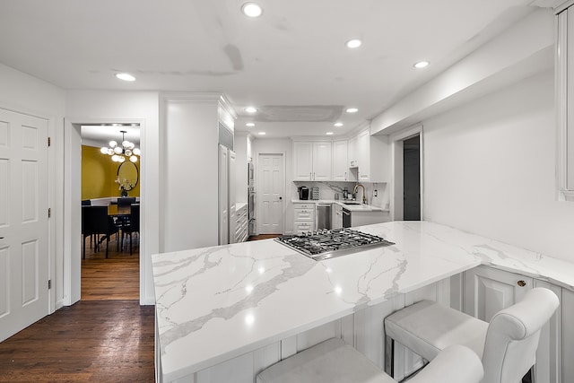 kitchen with a peninsula, a breakfast bar, a sink, white cabinets, and light stone countertops