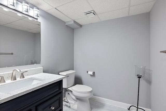 half bath featuring toilet, a paneled ceiling, vanity, visible vents, and baseboards