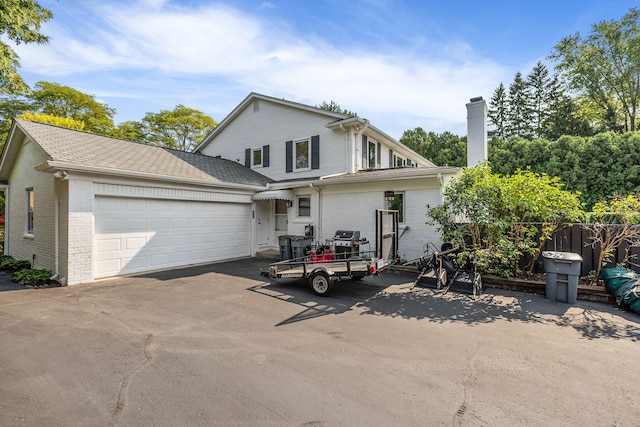 traditional-style home with aphalt driveway, brick siding, roof with shingles, a chimney, and an attached garage