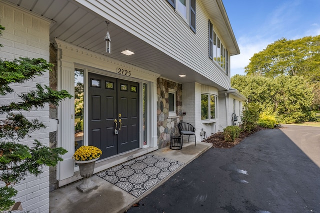 view of exterior entry featuring covered porch, stone siding, and brick siding