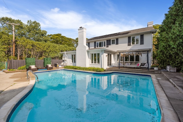 rear view of property with a patio area, a chimney, fence, and a fenced in pool