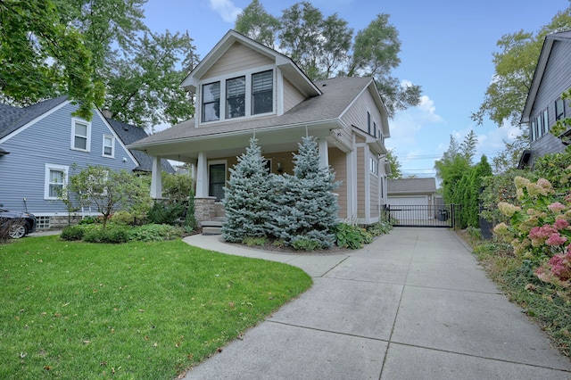 view of front of house with a porch, a front yard, a gate, and a detached garage