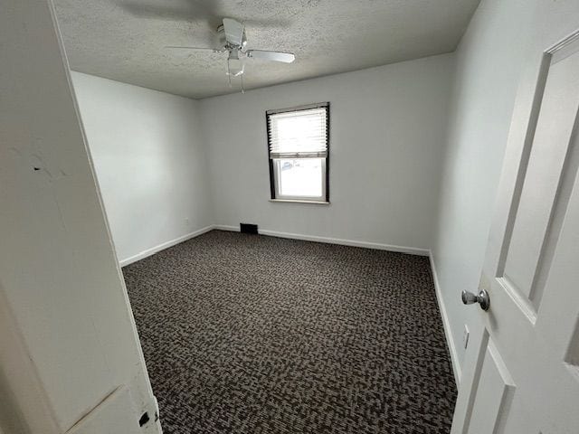 empty room with baseboards, dark carpet, ceiling fan, and a textured ceiling