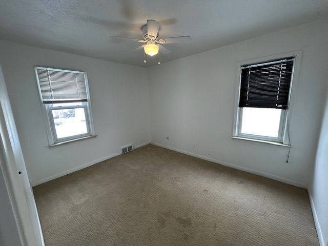 carpeted spare room with visible vents, baseboards, and a ceiling fan
