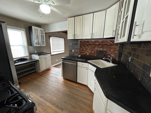 kitchen featuring a ceiling fan, stainless steel dishwasher, glass insert cabinets, a sink, and decorative backsplash