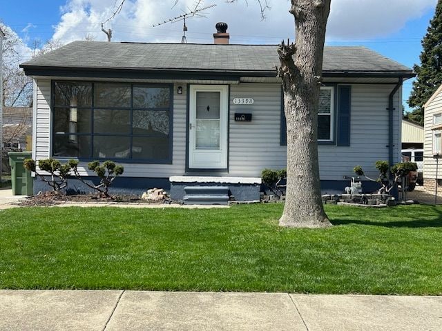 bungalow with a front lawn and a shingled roof