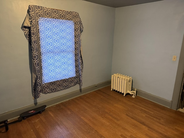 unfurnished room with baseboards, wood finished floors, and radiator