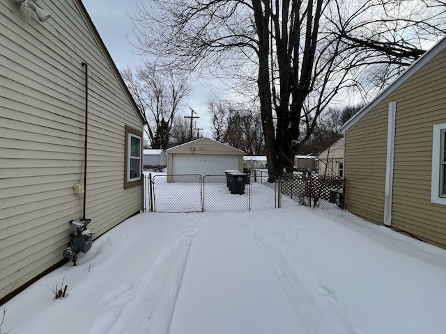 snowy yard with a garage, an outbuilding, and fence