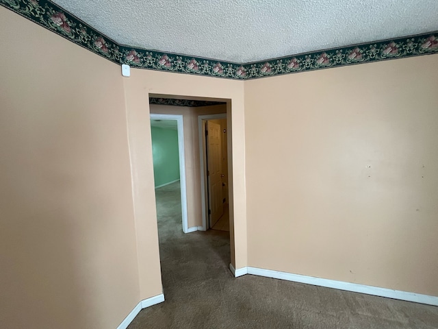 corridor featuring dark colored carpet, a textured ceiling, and baseboards