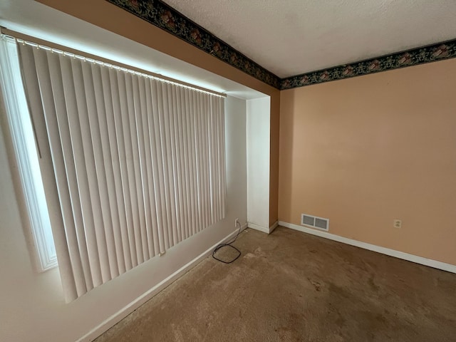 spare room featuring a textured ceiling, visible vents, and baseboards