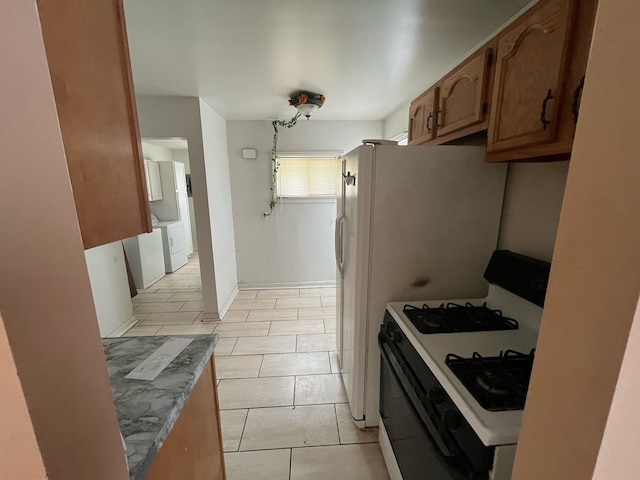 kitchen featuring light tile patterned floors, brown cabinetry, independent washer and dryer, light countertops, and white gas stove