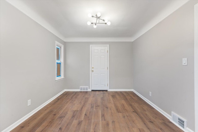 unfurnished room with a notable chandelier, wood finished floors, visible vents, and baseboards