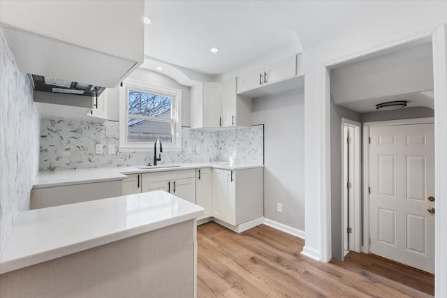 kitchen featuring a sink, light countertops, light wood-style floors, white cabinetry, and backsplash