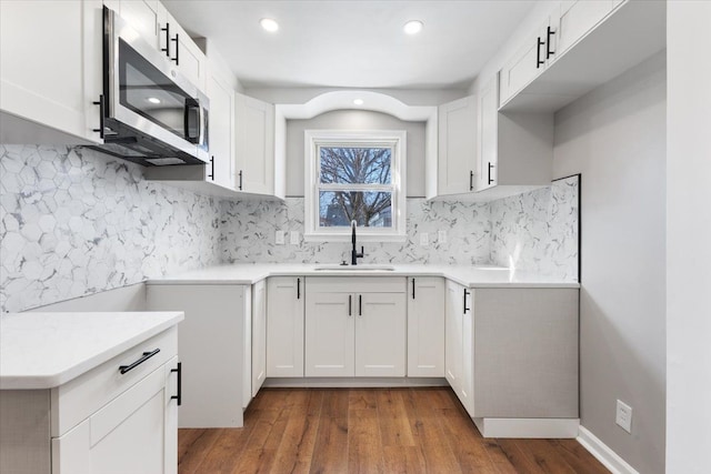 kitchen featuring light countertops, stainless steel microwave, dark wood-type flooring, white cabinetry, and a sink