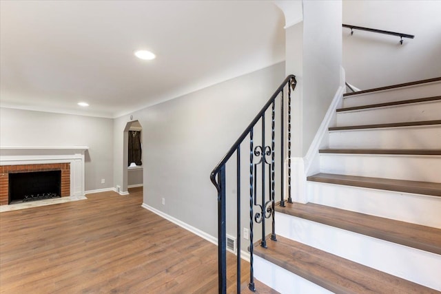 stairway featuring baseboards, arched walkways, wood finished floors, a brick fireplace, and recessed lighting