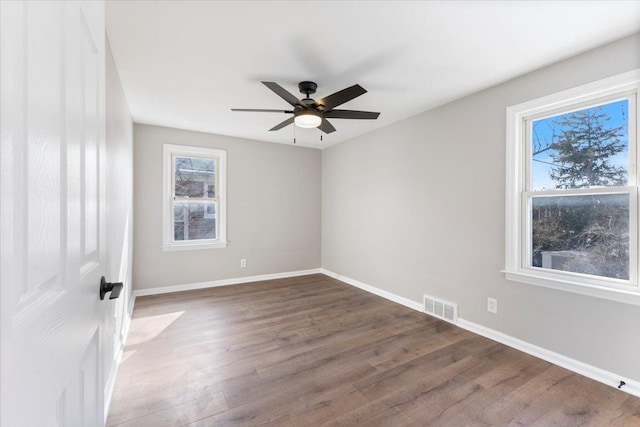 unfurnished room with dark wood-style floors, a ceiling fan, visible vents, and baseboards