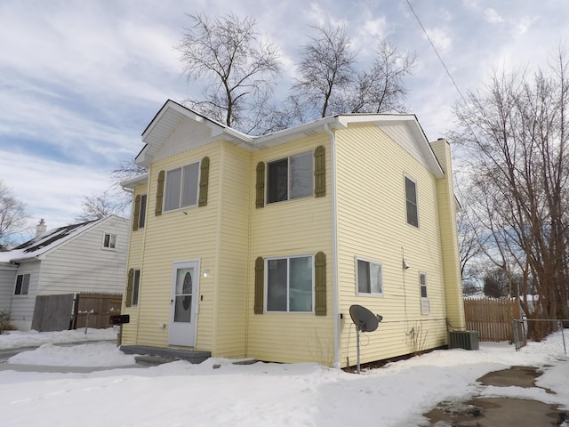 snow covered back of property with entry steps, fence, and a chimney